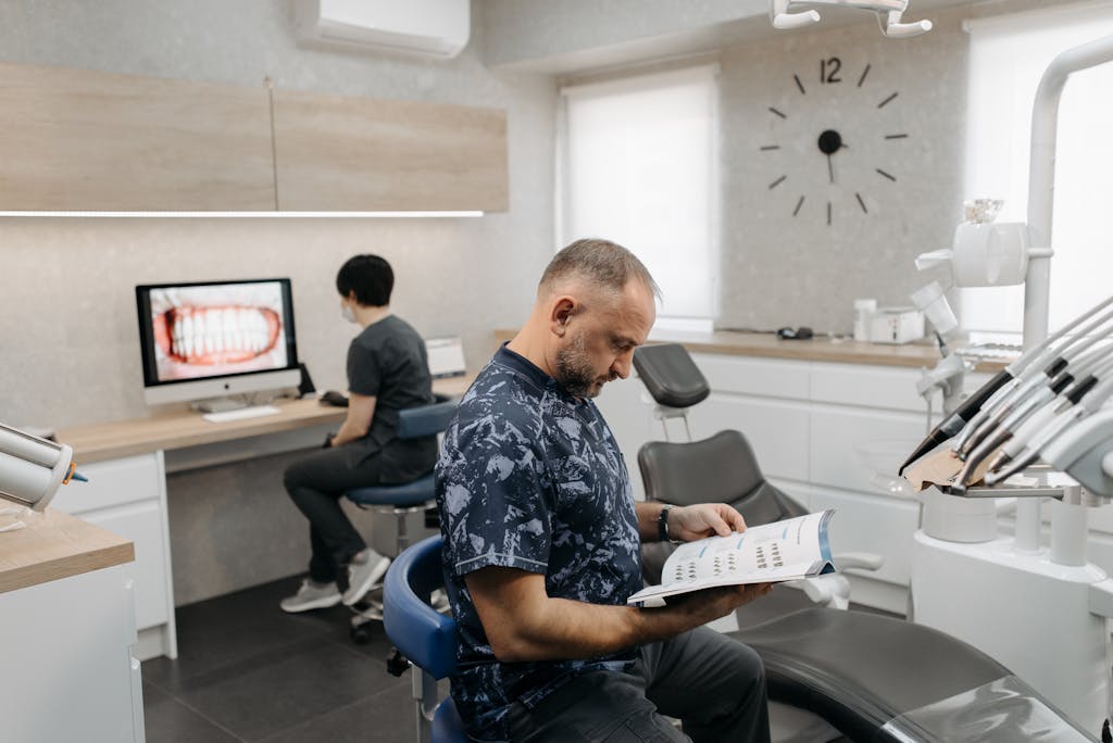 A dental professional reads a brochure while another works on a computer in a contemporary clinic.