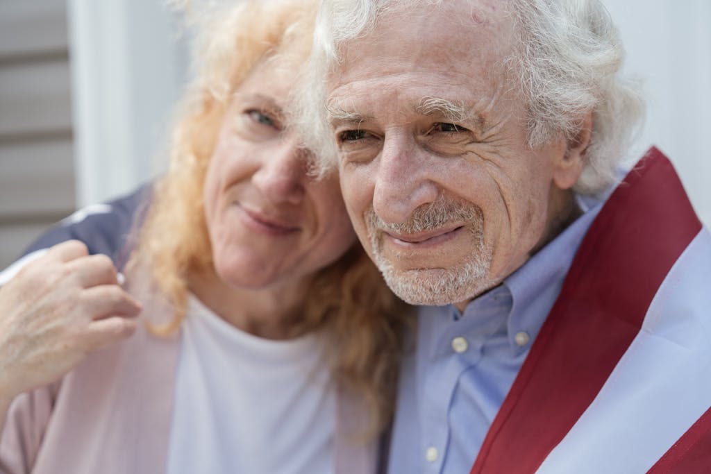 Happy senior couple wrapped in an American flag, symbolizing love and patriotism.
